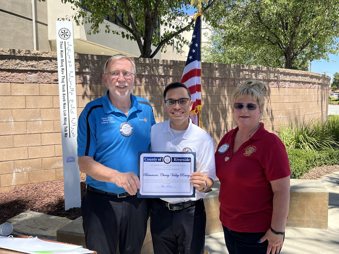 President Doug Emery accepts a Riverside County Certificate of Recognition from Supervisor Yxstian Gutierrez, beside the new Peace Pole and a U.S. flag