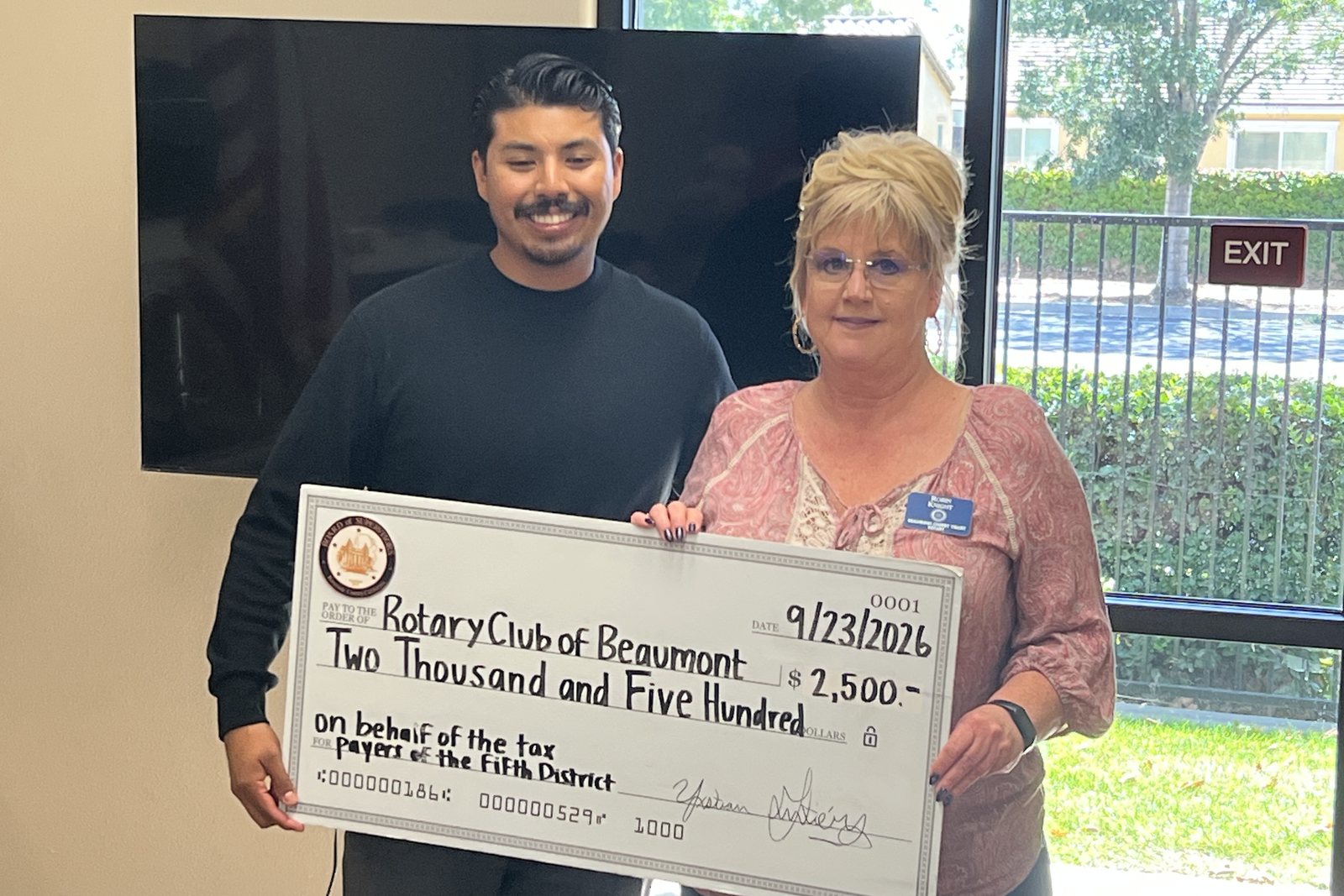 Robin Knight and a guest from Supervisor Yxstian Gutierrez's office hold an oversized check for two thousand five hundred dollars made out to the Rotary Club of Beaumont on behalf of the taxpayers of the Fifth District